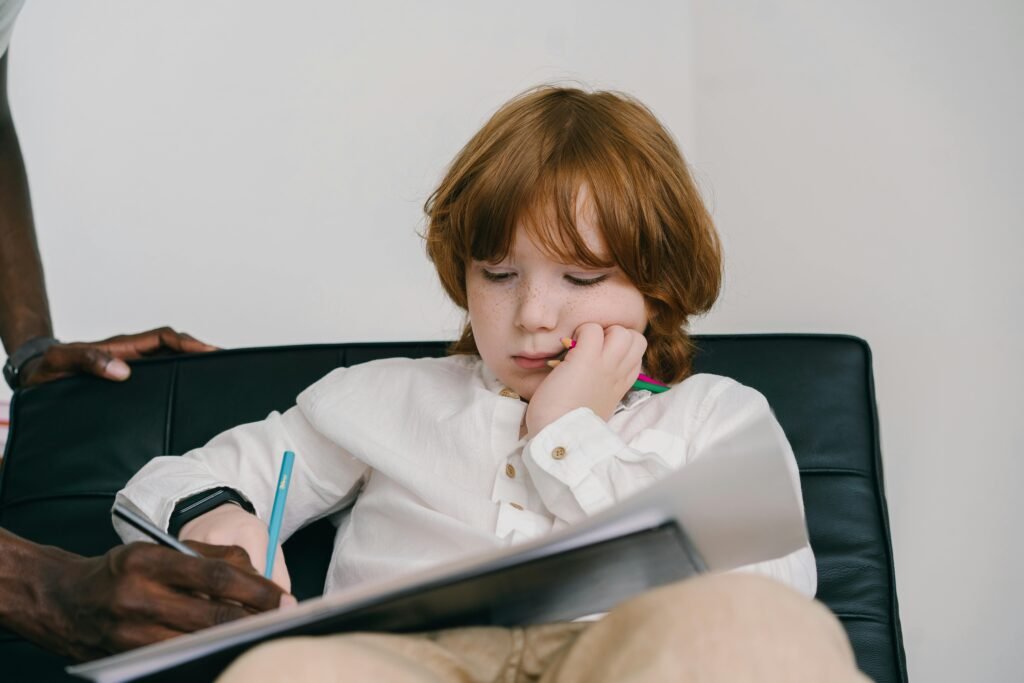 Young boy with freckles focused on drawing during an education session indoors.